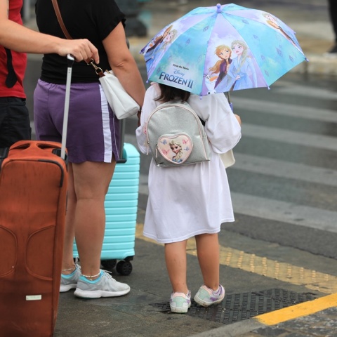 Παιδάκι κρατά ομπρέλα εν μέσω βροχής και περιμένει κοντά σε διάβαση πεζών