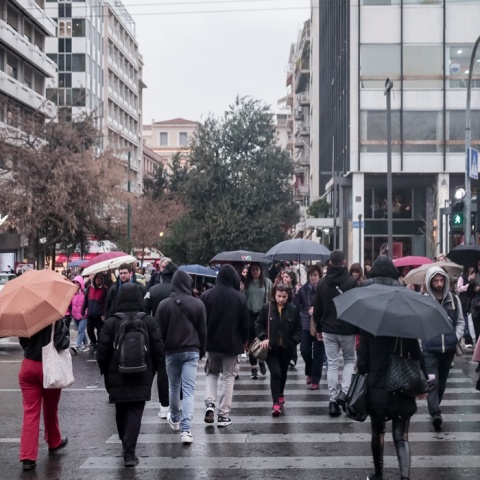 Πολίτες στο Σύνταγμα κρατούν ομπρέλα και περπατούν στον δρόμο υπό βροχή