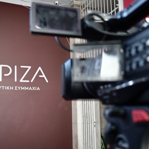 Το λογότυπο του ΣΥΡΙΖΑ και δίπλα κάμερα τηλεοπτικού συνεργείου