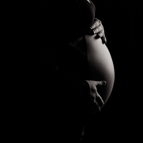 Κοιλία εγκυμονούσας γυναίκας που φωτίζεται ενώ γύρω γύρω υπάρχει σκοτάδι