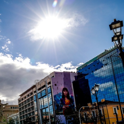 Ήλιος και λιγοστά σύννεφα πάνω από κτίρια στο κέντρο της Αθήνας