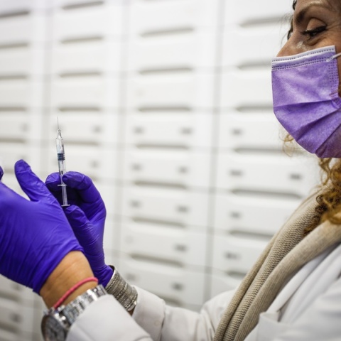 Γυναίκα κρατά εμβόλιο και βαμβάκι στα χέρια της