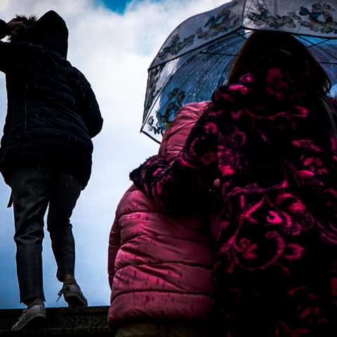 Γυναίκα με ομπρέλα κρατά κοντά της το παιδί της για να μην βραχεί όσο ανεβαίνουν σκάλες