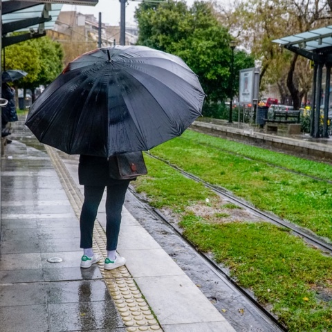 Άτομο με ομπρέλα περιμένει σε στάση του τραμ