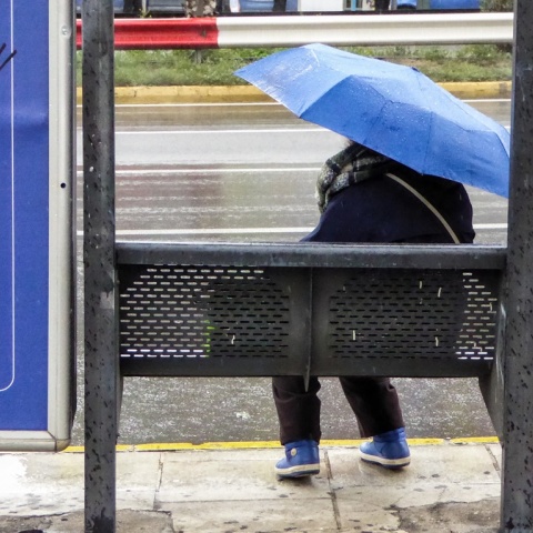 Γυναίκα με ομπρέλα σε στάση λεωφορείου ενώ βρέχει