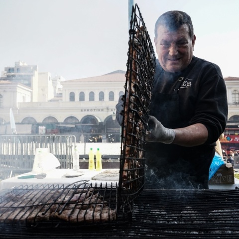 Ψήστης γυρνά τις σχάρες με τα κοψίδια σε υπαίθριο ψήσιμο την Τσικνοπέμπτη