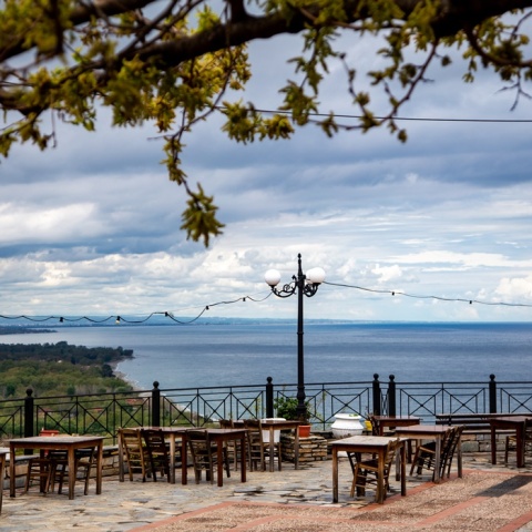 Συννεφιασμένος καιρός και υπαίθρια ταβέρνα με τραπεζάκια σε μπαλκόνι με θέα