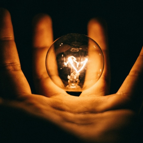 Αναμμένη λάμπα ανάμεσα στα δάχτυλα ενός χεριού