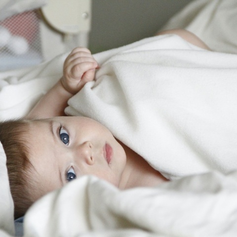 Μωρό με γαλανά μάτια κοιτά στην κάμερα ενώ είναι τυλιγμένο με σεντονάκι