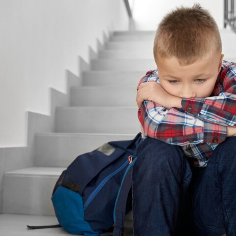 Παιδί κάθεται στα σκαλιά με την τσάντα του δίπλα και έχει ακουμπήσει το κεφάλι του στα γόνατά του - Εικόνα που παραπέμπει σε βία στα σχολεία - bullying