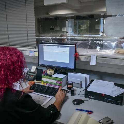 Γυναίκα με κόκκινα μαλλιά πλάτη στον φακό σε υπηρεσία συντάσσει φορολογική δήλωση στον υπολογιστή της