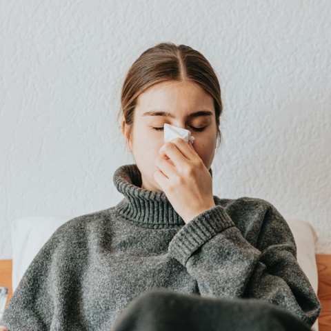 Γυναίκα ξαπλωμένη στο κρεβάτι με ίωση που φυσά τη μύτη της
