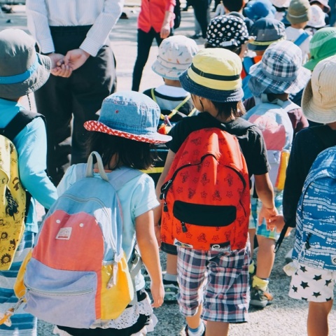 Παιδιά με καλοκαιρινά ρούχα και τσάντες στην πλάτη περπατούν πιασμένα χεράκι - χεράκι
