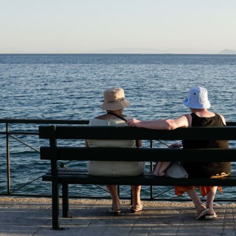 Ηλικιωμένοι κάθονται σε παγκάκι μπροστά στη θαλάσσα