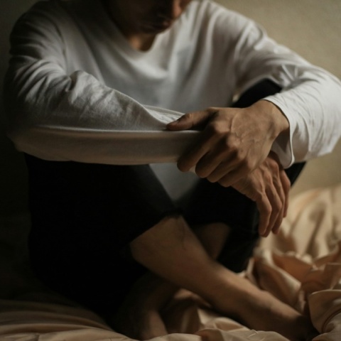 Άτομο καθισμένο στο κρεβάτι που πιάνει με τα χέρια του, τα πόδια του