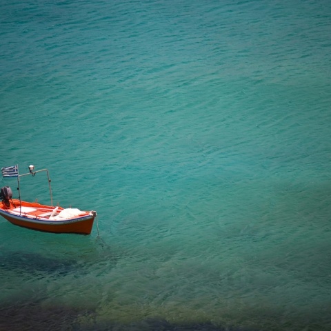 Παραλία και καΐκι αγκυροβολημένο που έχει στην πλώρη του την ελληνική σημαία