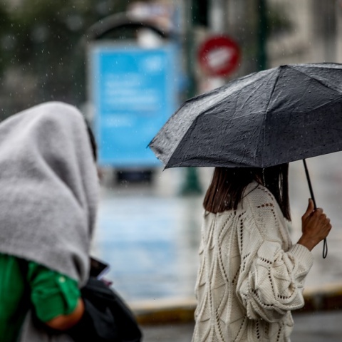 Γυναίκα με ομπρέλα προστατεύεται από τη βροχή - Άτομο έχει ρίξει ρούχο στο κεφάλι του για να μην βραχεί