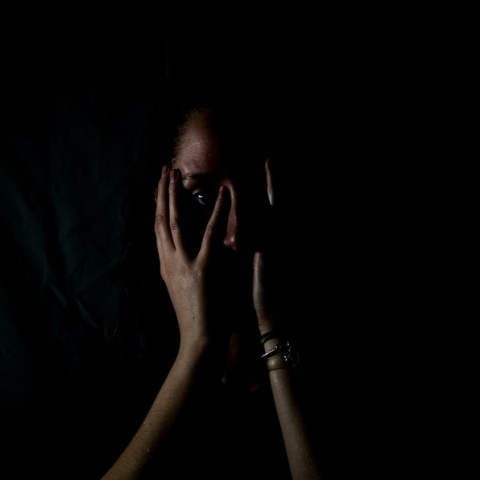 Γυναίκα που κλαίει κρατά το πρόσωπό της ενώ βρίσκεται στο ημίφως - Εικόνα που παραπέμπει σε κακοποίηση και ενδοοικογενειακή βία