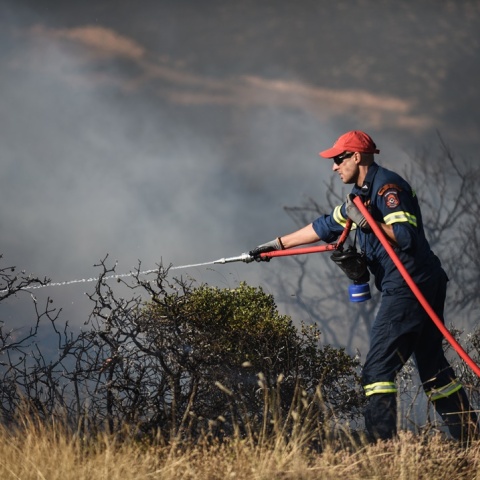 Πυροσβέστης με μάνικα ρίχνει νερό σε περιοχή όπου έχει περάσει φωτιά για τον κίνδυνο αναζωπυρώσεων