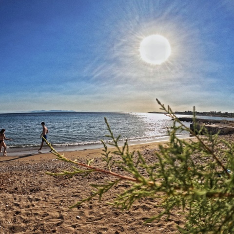 Ακτίνες του ήλιου πέφτουν στον φωτογραφικό φακό ενώ τραβά σκηνή από παραλία με αμμουδιά και δύο άτομα με μαγιό να βρίσκονται στην ακρογυαλιά