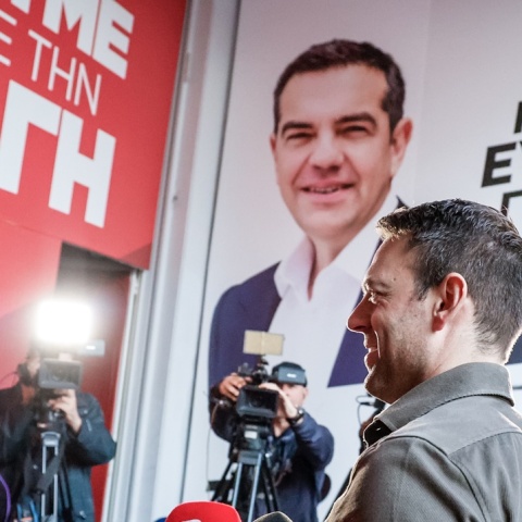 Ο Στέφανος Κασσελάκης προχωρά σε κτίριο που στο εξωτερικό του έχει αφίσα του ΑΛέξη Τσίπρα