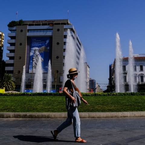 Γυναίκα εν μέσω καύσωνα περπατά μπροστά από το σιντριβάνι της Ομόνοιας