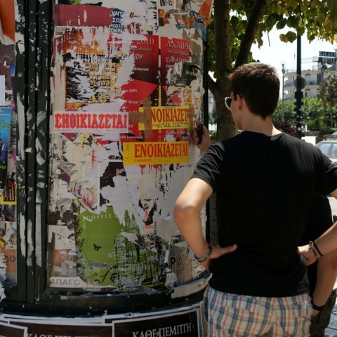 Ενοικιαστήρια σε κολώνα και νεαρό άτομο που κοιτά ενοικιαστήρια