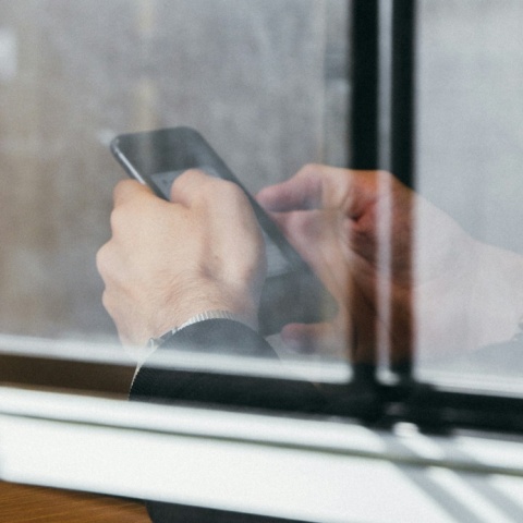 Άνδρας πίσω από τζάμι κρατά και πληκτρολογεί στο κινητό του τηλέφωνο