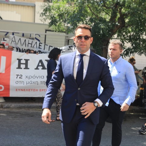 Ο Στέφανος Κασσελάκης περπατά μπροστά από πανό διαμαρτυρίας για την «Αυγή»