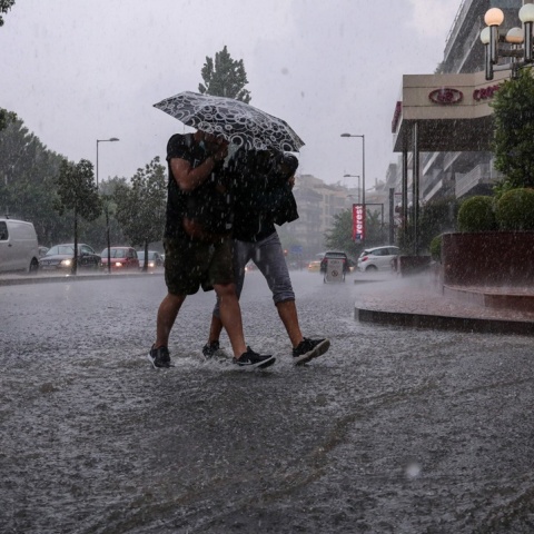 Άτομα προστεύονται από την καταρρακτώδη βροχή με ομπρέλα