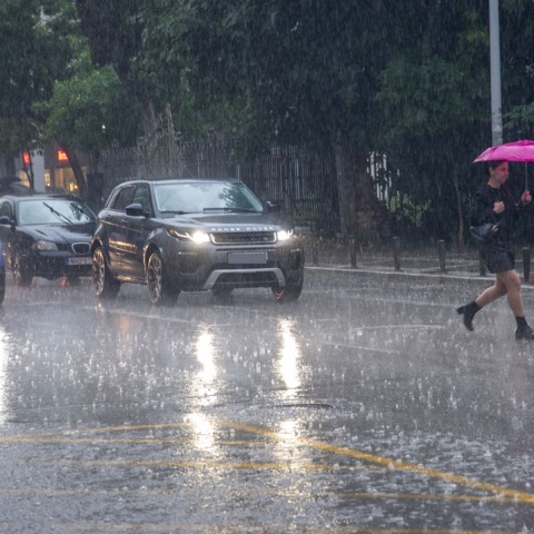 Γυναίκα με ομπρέλα διασχίζει δρόμο υπό καταρρακτώδη βροχή