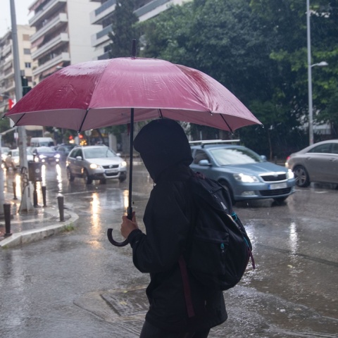 'Άτομο με ομπρέλα και κουκούλα προστατεύεται από ισχυρή καταιγίδα