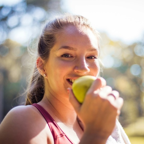 Γυναίκα τρώει φρούτο και κοιτά τον φακό