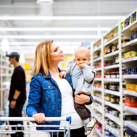 Γυναίκα με καρότσι του σούπερ μάρκετ και το μωρό στην αγκαλιά της