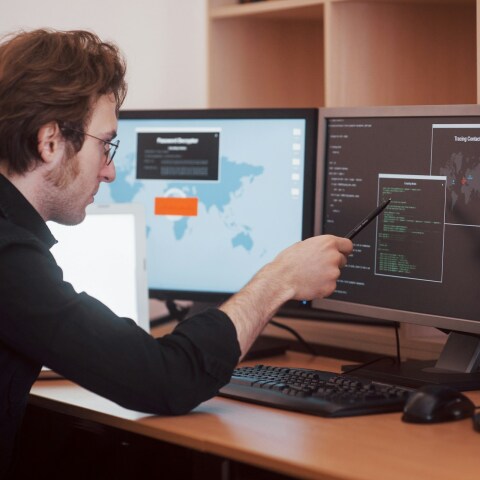 Άτομο διαβάζει κώδικα μπροστά από οθόνες υπολογιστή