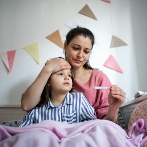 Κοριτσάκι με πυρετό στο κρεβάτι με τη μαμά του που του μετρά τη θερμοκρασία