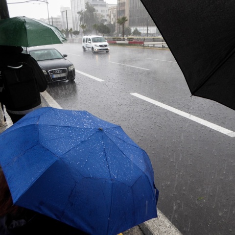 Άτομο με ομπρέλα περιμένουν εν μέσω βροχής σε στάση λεωφορείου 