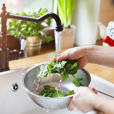 Άτομο πλένει σπανάκι κάτω από το νερό της βρύσης