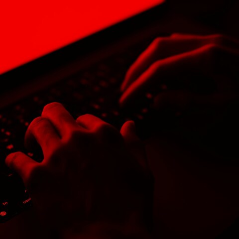 Άτομο σε σκοτεινό κόκκινο φόντο πληκτρολογεί - Εικόνα που παραπέμπει στη δράση χάκερ