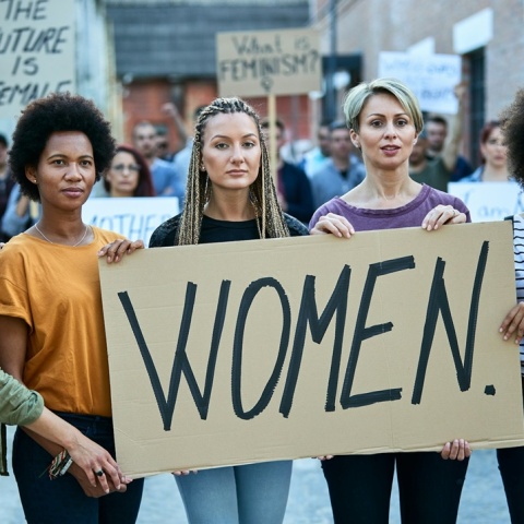 Γυναίκα με χαρτόνι που γράφει στα αγγλικά τη λέξη «Γυναίκες»