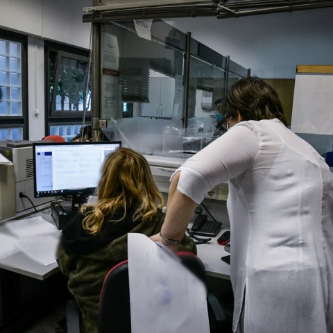 Γυναίκα σε υπολογιστή στην υπηρεσία της και από πάνω της μία άλλη γυναίκα που της δίνει οδηγίες