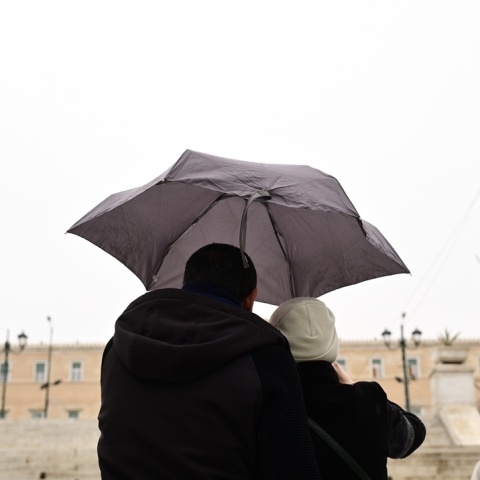 Πολίτες με ομπρέλα προστατεύονται από τη βροχή μπροστά από τη Βουλή