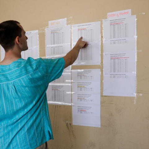 Άτομο μπροστά από τις βαθμολογίες των μαθημάτων των Πανελληνίων που είναι ανηρτημένες έξω από σχολείο