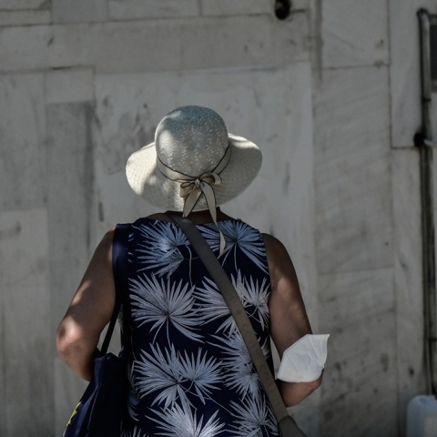 Γυναίκα με γυρισμένη πλάτη στον φακό και τη μάσκα προστασίας από τον κορωνοϊό αφημένη στον αγκώνα