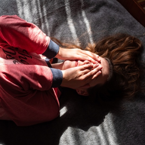 Κορίτσι που κρύβει το πρόσωπό του ενώ είναι ξαπλωμένο σε κρεβάτι