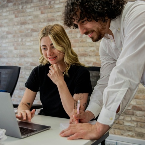 Εργαζόμενος κοιτά σε υπολογιστή πάνω από άλλη εργαζόμενη που κοιτά σε υπολογιστή