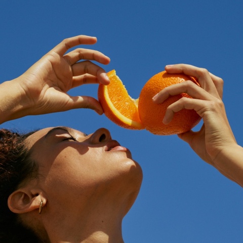 Κοπέλα στον ήλιο με κομμένο πορτοκάλι πάνω από το πρόσωπό της