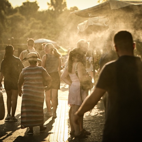 Πολίτες περπατούν υπό υψηλές θερμοκρασίες δίπλα σε σύστημα που βράζει σταγόνες νερού για δροσιά