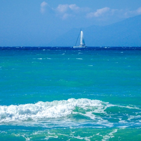 Κυματάκια σε παραλία και στο βάθος ένα ιστιοφόρο