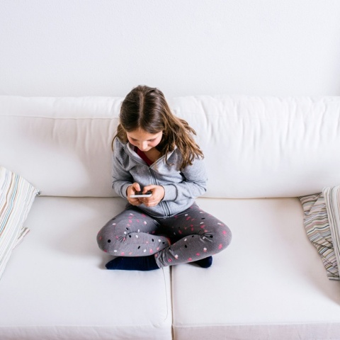 Παιδί καθισμένο σε καναπέ με το κινητό στο χέρι